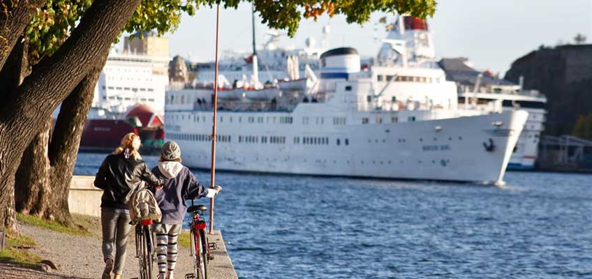 Personer leder cyklar vid en kanal med skepp i